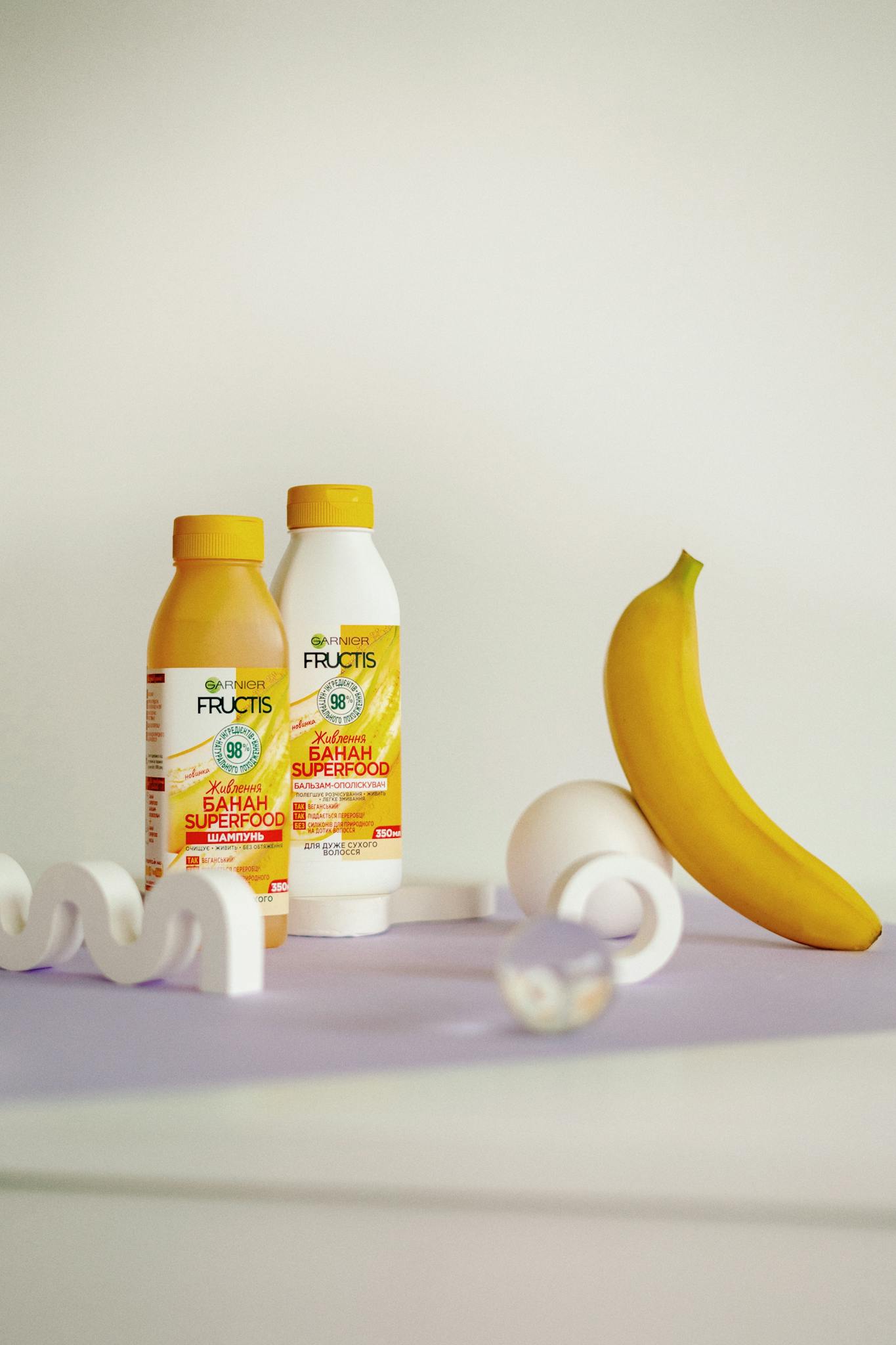 Colorful arrangement of superfood bottles with a banana on a pastel surface, ideal for health and wellness themes.