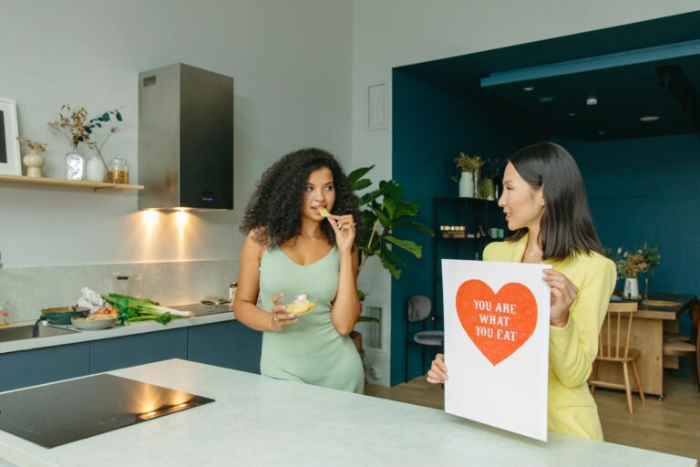 Two women discussing nutrition in a kitchen, holding health-related posters.